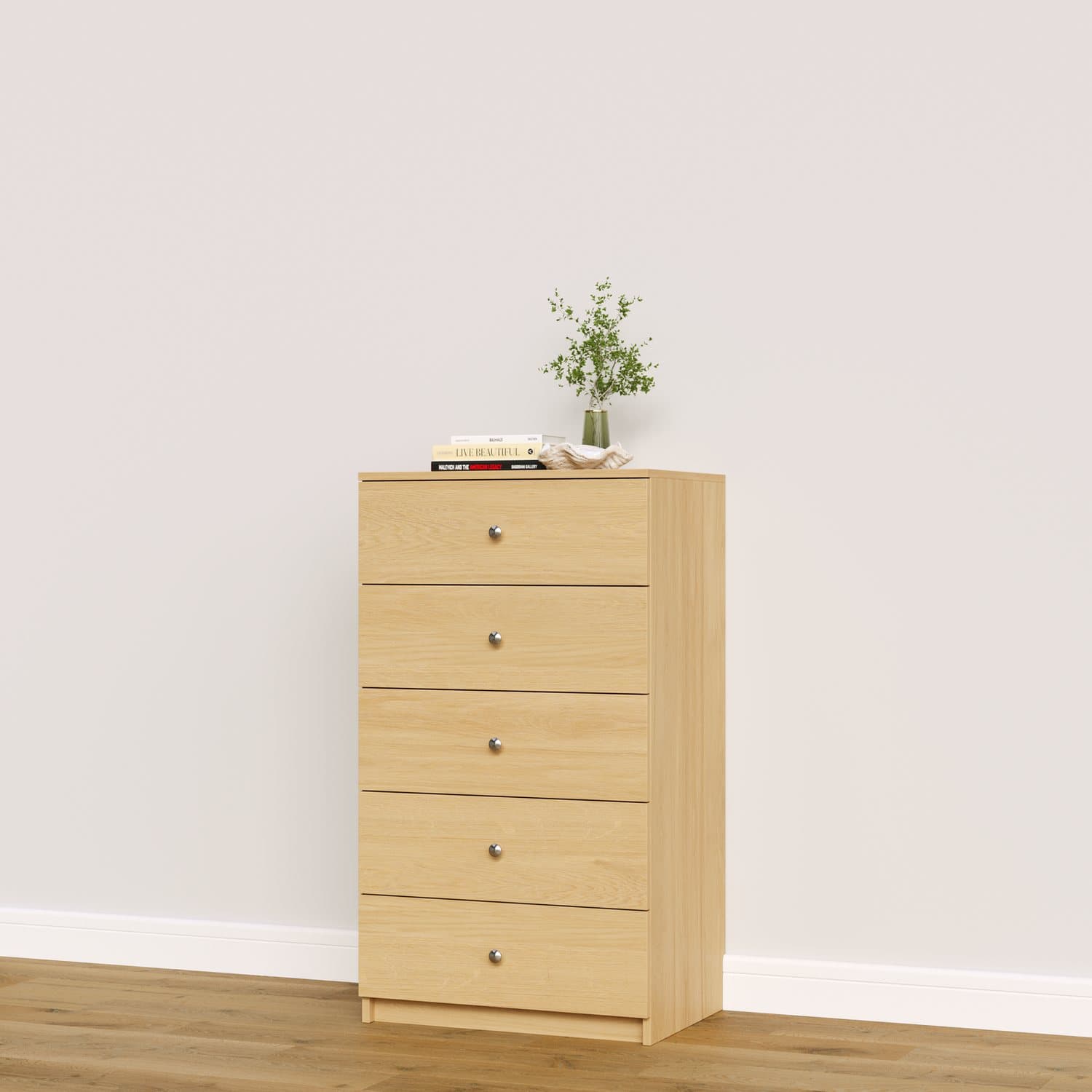 A five-drawer chest in natural oak standing against a wall, with a plant and a book on top.